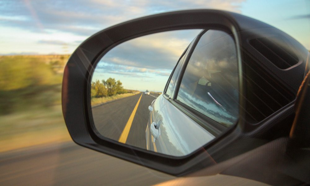 Blog - Car Review Driver Mirror with a View of the Road Behind Car on a Nice Day