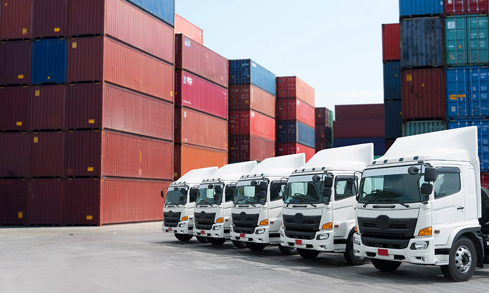Blog - Fleet of White Trucks in front of Storage Containers in a Large Log
